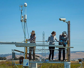 Three female researchers install equipment on a monitoring tower in the Sacramento-San Joaquin Delta.