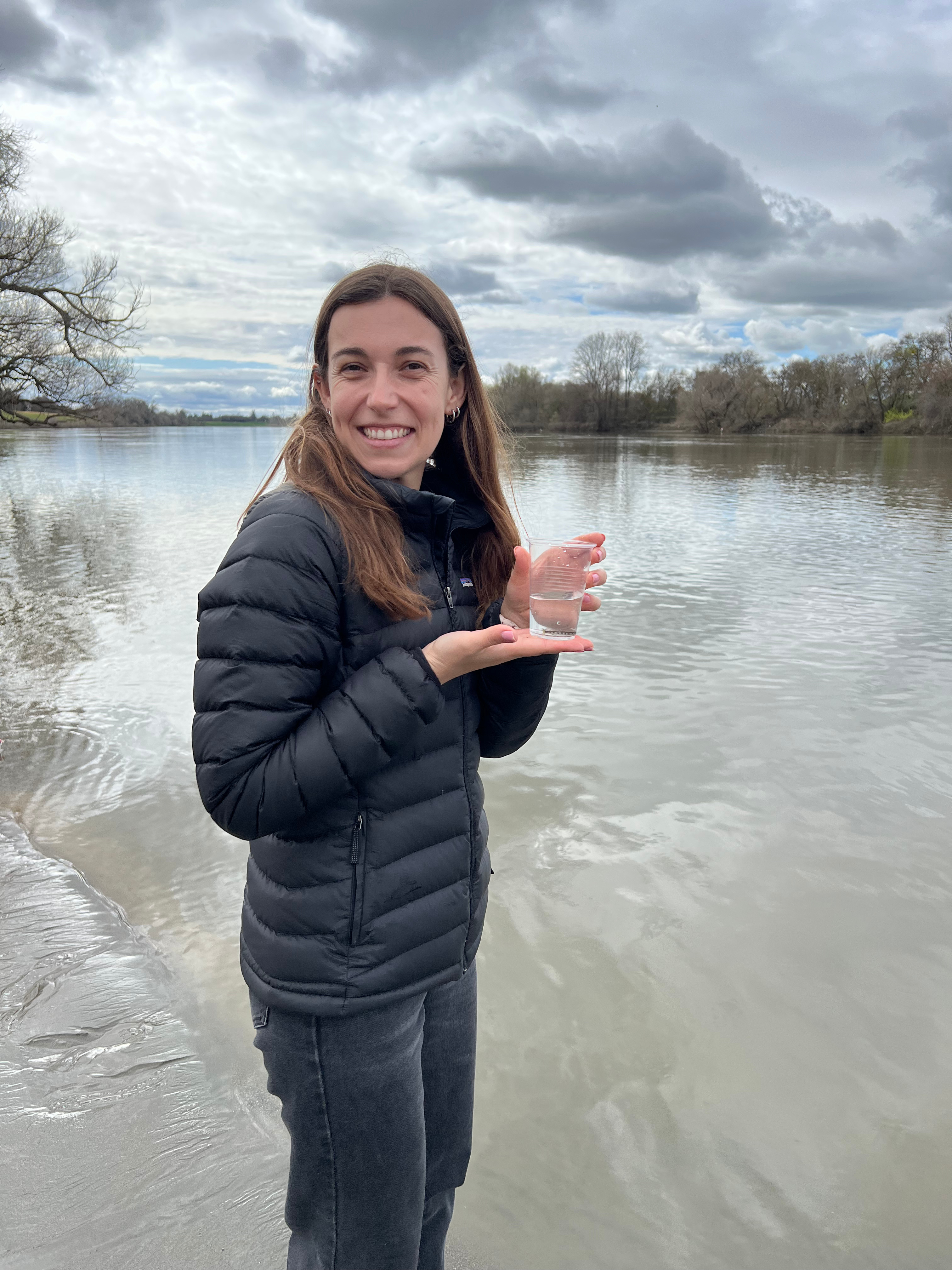 Becca VanArnam holding a juvenile live salmon beside the Sacramento River during a student salmon release field trip.