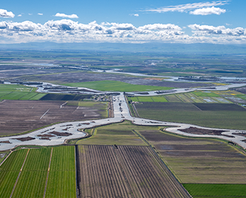 An aerial photo of farmland and waterways in the Sacramento-San Joaquin Delta with rolling hills and sky in the background.